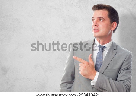 Business man with grey suit. He is pointing to something. Over concrete wallpaper