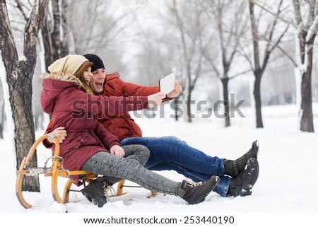 Young couple in love on a winter vacation sitting on a sleigh and making selfie
