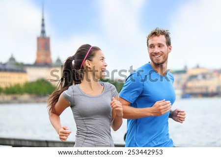 Healthy runners running in Stockholm city cityscape background. Riddarholmskyrkan church in the background, Sweden, Europe. Healthy multiracial young adults, asian woman, caucasian man. Royalty-Free Stock Photo #253442953