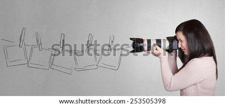 Young beautiful and pretty photographer woman taking a picture with dslr camera on grey wall background with empty photo frames with place for your text or drawing
