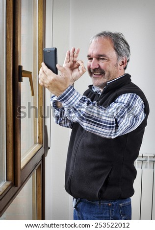Mature man does ok signal while taking a picture with mobile phone