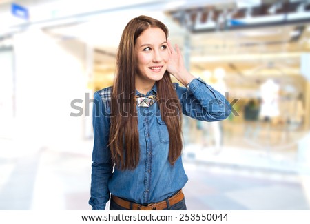 Trendy young woman paying attention with her hand on her ear. Over shopping center background