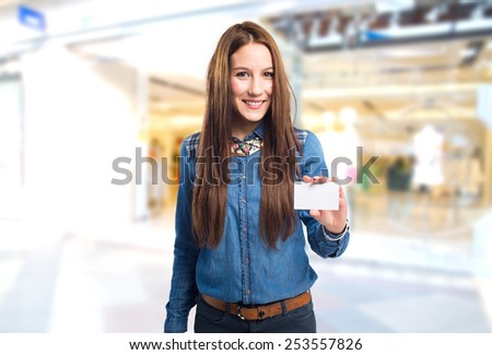 Trendy young woman smiling and holding a white card. Over shopping center background