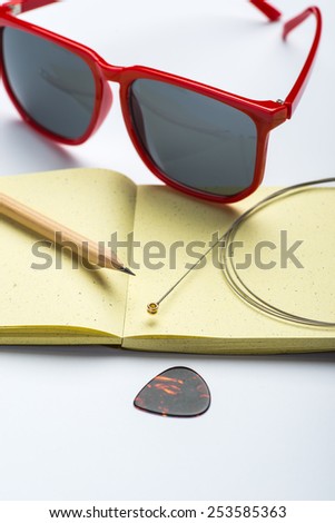 Yellow notepad with pencil, sunglasses, string and mediator on white surface