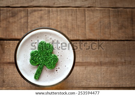 St. Patricks Day Shamrock Floating in Frothy Beer Mug on rustic wood board background with room or space for copy, text, your words.  Closeup Above View Horizontal with warm tone 