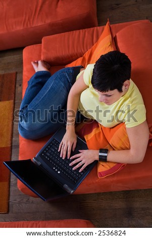 Young woman is sitting and resting on the sofa and using a laptop computer. Maybe she is surfing the net, chatting or studying for the next university exam.