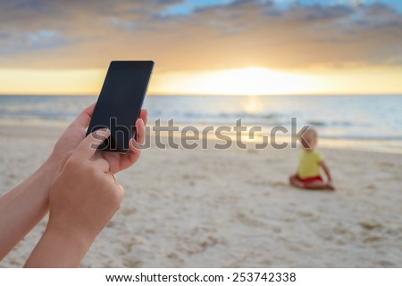 Woman is taking pictures of her son on the beach during warm sunset