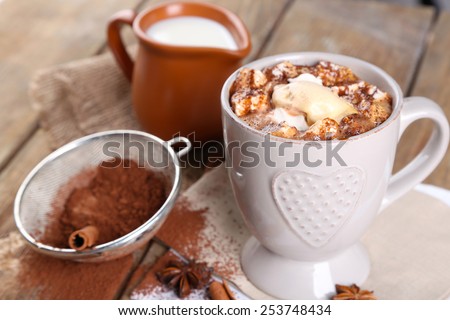 Cup of hot coffee with marshmallow and cup of milk with cinnamon, star anise and strainer of cocoa on napkin and rustic wooden table background