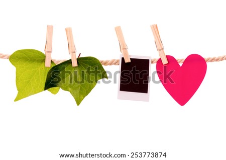 green leaves heart paper shape and instant photo hanging on a rope clothesline isolated on white