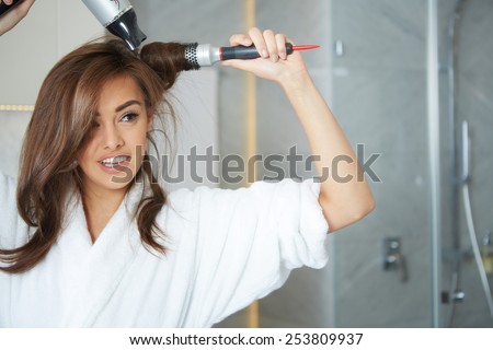 Young woman blow drying hair in bathroom Royalty-Free Stock Photo #253809937