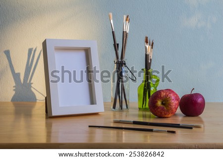 White photo frame and paintbrush in the glass bottles on wooden table over grunge background