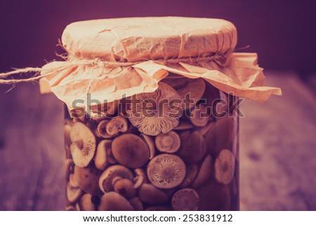 Vintage photo of preserved food in glass jar, on a wooden shelf. Marinaded mushrooms