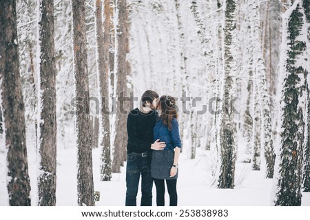 Young happy couple kissing and hugging in the winter snowy forest
