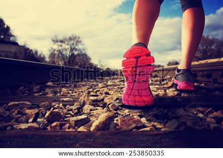 woman running down railroad tracks during the sunlight with retro instagram filter (shallow depth of field)