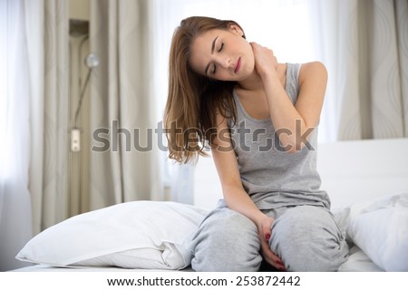 Young woman sitting on the bed with pain in neck Royalty-Free Stock Photo #253872442