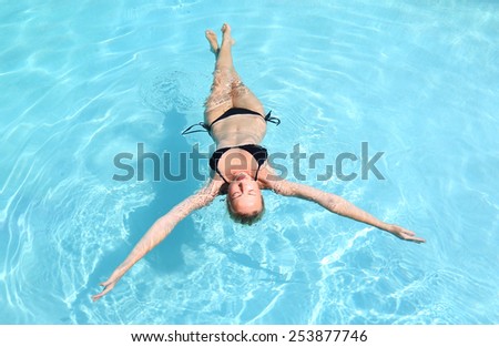 Beautiful Caucasian woman floating in turquoise blue swimming pool.