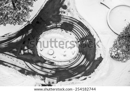 Black and white view from above of winter scene with trees, car traces and steps on snow, multiple circle shapes, graphic contrast design