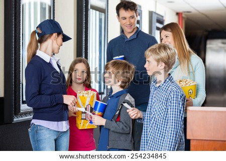 Young female worker checking movie tickets of family at cinema