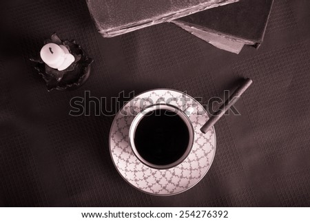 Old books, cup of coffee, cigarette and ancient candle on the red tablecloth. Toned.