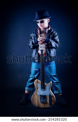 Portrait of a boy posing with his guitar, over black background. 