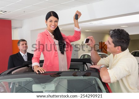 Woman standing in red cabriolet and man taking picture at new car showroom