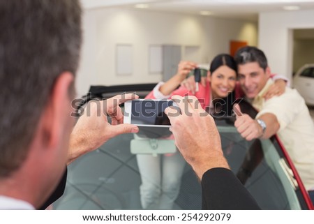 Businessman taking picture of the couple in their new car at new car showroom