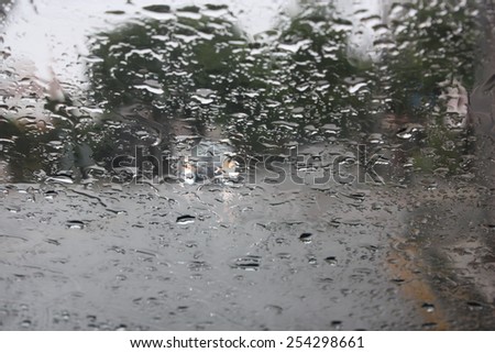 Raindrops on a glass window with blurry trees, road and car