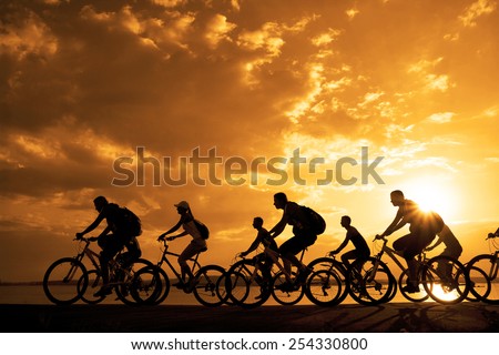 Image of sporty company friends on bicycles outdoors against sunset. Silhouette A lot phases of motion go of nine 9 cyclist along shoreline coast Reflection sun on water Copy Space for inscription