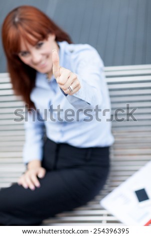 Photo of caucasian businesswoman sitting on a metal bench and making positive thumb gesture