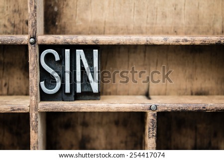 The word "SIN" written in vintage metal letterpress type in a wooden drawer with dividers.