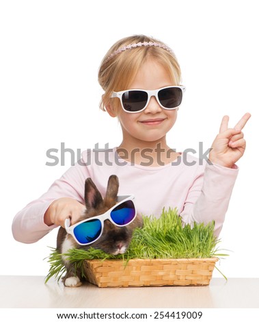 Photo of little smiling girl showing victory sign and brown bunny in sunglasses, isolated on white