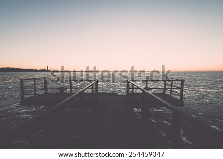 sunset over frozen sea with ice blocks and dramatic colorful sky with old metal bridge - vintage retro grainy film effect