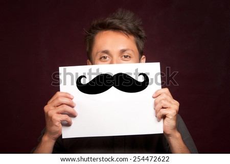 Young man with a happy smiley card half covering face with large false mustache like a hipster