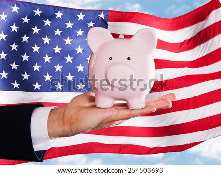 Businessman Holding Piggybank In Front Of Usa Flag