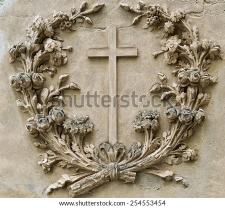 cross in the center of a garland of flowers made on an ancient wall