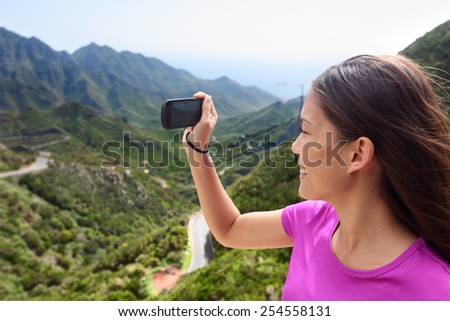 Girl taking smartphone picture of mountain nature. Female tourist traveling on road trip or hike in mountainous Anaga of Tenerife, Canary islands. Summer vacations.