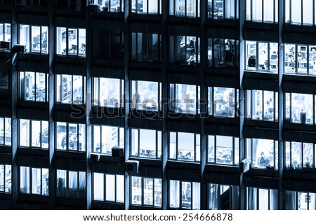 Modern office building with glowing windows at night, black and white toned in blue