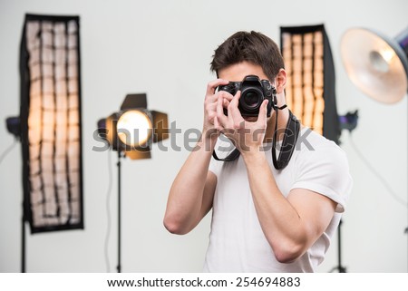 Young smiling photographer with camera in professionally equipped studio.
