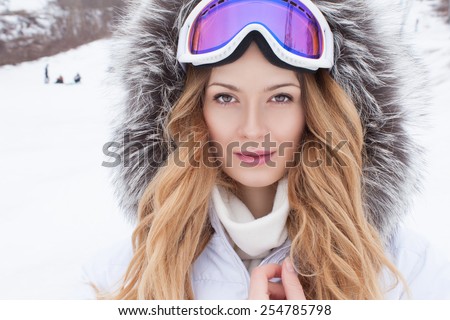 Close-up Portrait Beautiful Model Woman wearing a Snowboard Mask on her Head. Attractive Model Woman Blonde wearing a Ski Mask sitting in the Snow. Model rests in  Winter with Snowboarding         
 