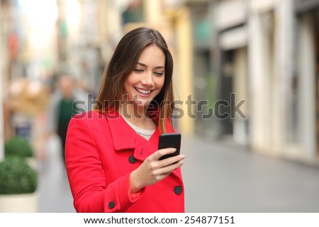 Girl walking and texting on the smart phone in the street wearing a red jacket in winter
