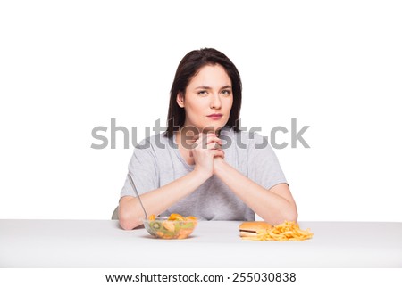 picture of woman with fruits and hamburger in front thinking about choice on white background, healthy versus junk food concept