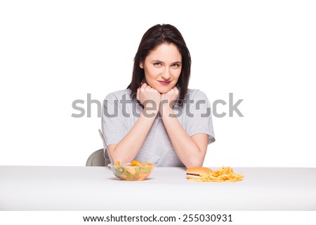healthy versus junk food concept with a natural woman heaving in front fruits meal and fries with hamburger, isolated on white
