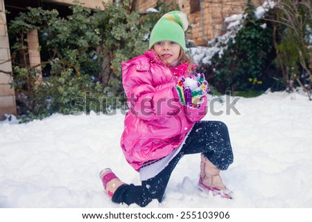 Little cute girl standing on one knee in the snow with a snowball in her hands