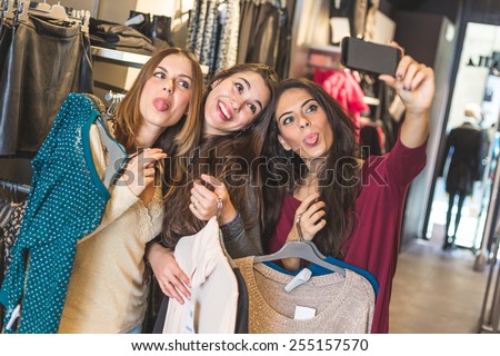 Three women taking a selfie while shopping in a clothing store. They are happy and smiling at camera. Shopping concept, also related to social media addiction.