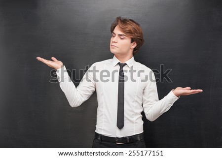 Photo of casual young man with his two palms up on blank chalkboard background. Man with one hand above making a choice
