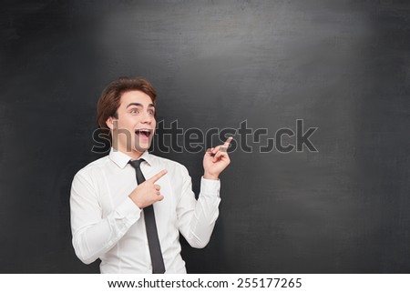 Photo of handsome funny young man on blank chalkboard background. Man pointing at chalkboard