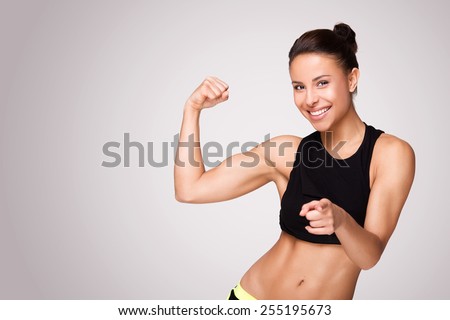 Cheerfully smiling mixed race sporty woman demonstrating biceps, isolated on white background Royalty-Free Stock Photo #255195673