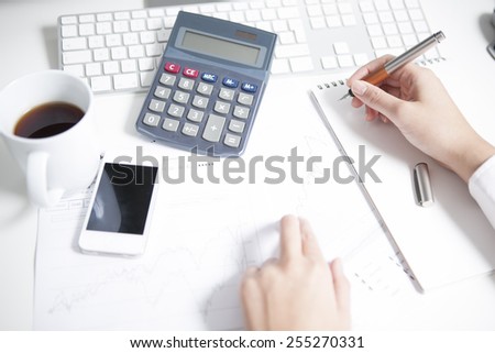 Woman working at desk, smart phone, notepad, calculator