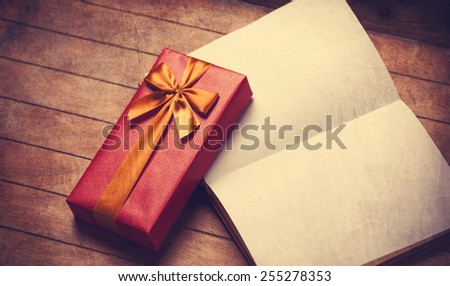 Opened book and gift box on a wooden table. Photo in old color image style.