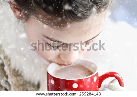 Young girl dressed warmly, drinking hot chocolate outdoor in the winter. Selective focus on child's eyes with extreme shallow depth of field.